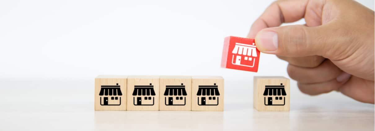 Wooden blocks depicting business locations with a hand placing a red block with the same image within the line