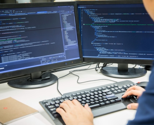 Male computer programmer sat with two screens showing lines of code