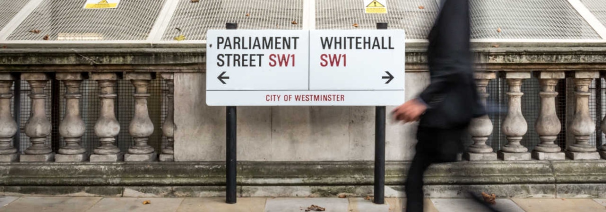 London civil servant. A suited office worker passing a street sign for Parliament Street and Whitehall in the civil service district of Westminster.